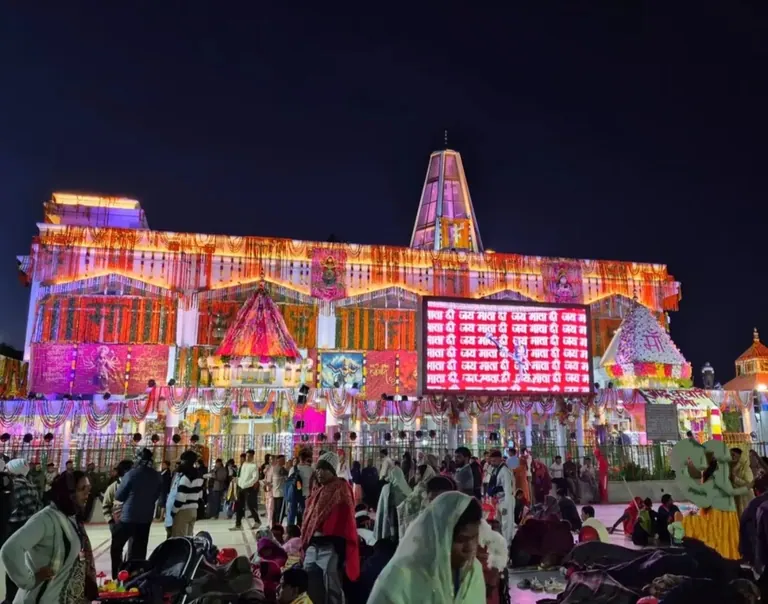 The temple at Adhkuwari decorated with coloured lights at night, with pilgrims in the courtyard