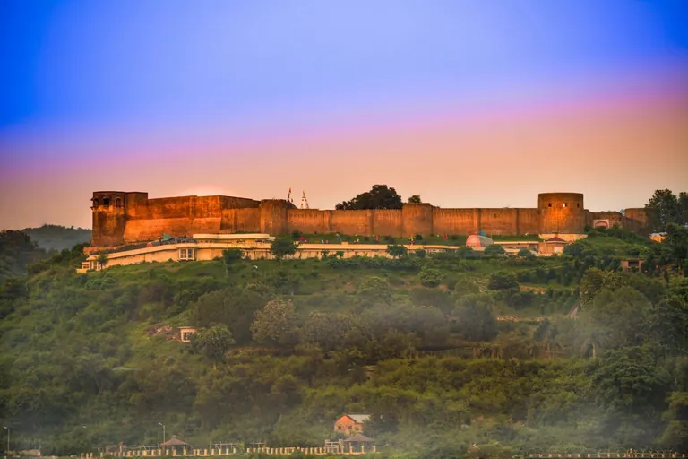 The long walls of Bahu Fort on a wooded ridge in Jammu glowing at dusk