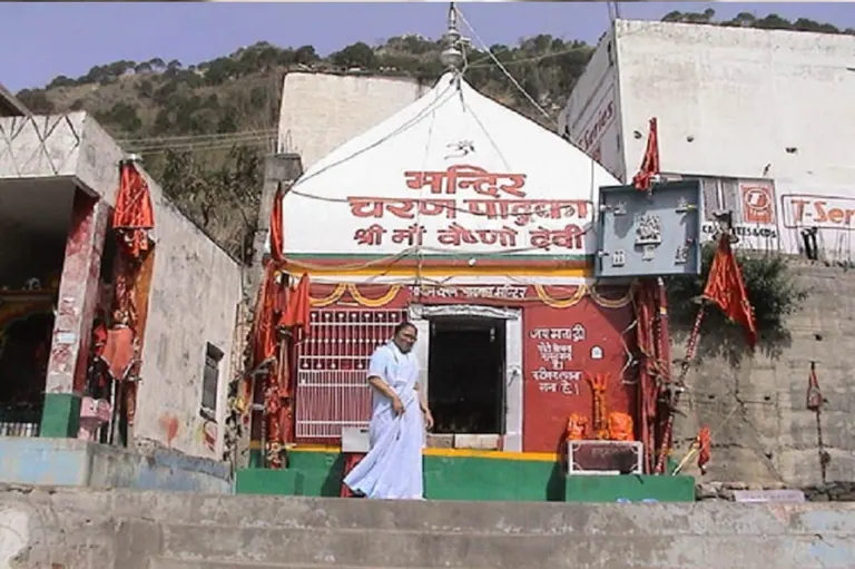 The small Charan Paduka shrine on the Vaishno Devi route with flags and a pilgrim at the entrance, photographed in the 1990s