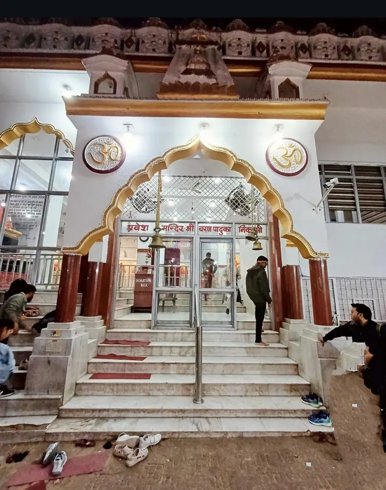 Arched marble entrance of the Charan Paduka temple on the Vaishno Devi route with pilgrims on the steps