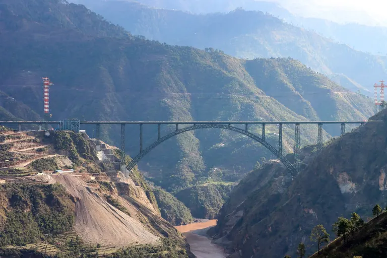 The steel arch of the Chenab rail bridge spanning a deep river gorge between mountains in Reasi district