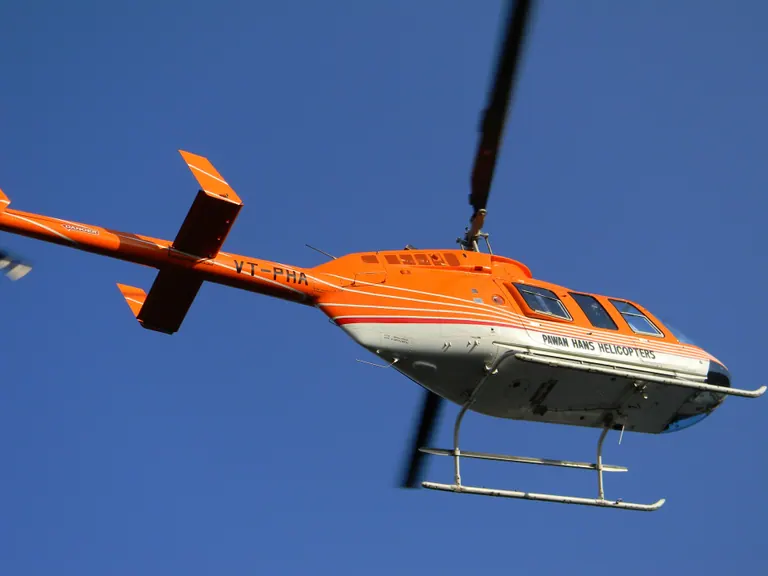 An orange and white helicopter climbing against a clear blue sky