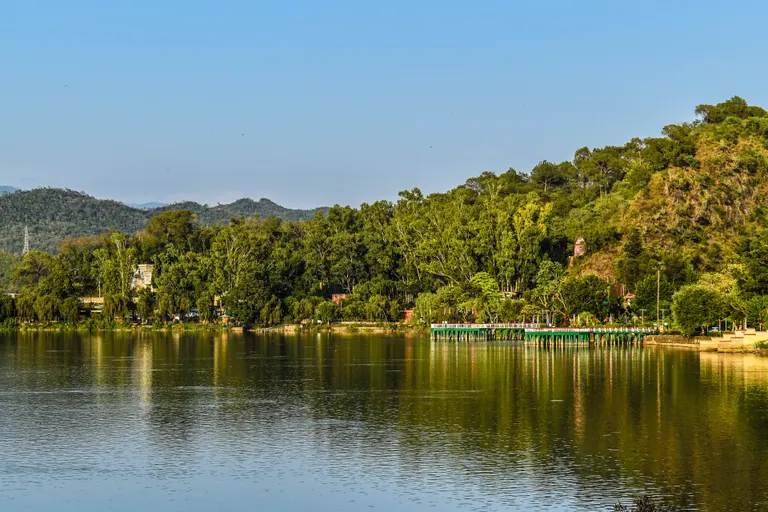 Calm waters of Mansar Lake reflecting the forested hills around it
