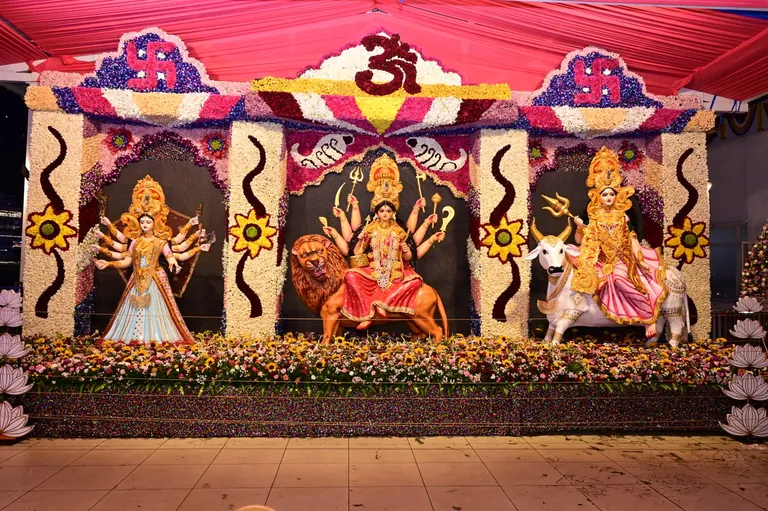 A floral Navratri decoration with idols of the Goddess, seated on a lion in the centre and on a bull on the right, under arches of flowers with Om and swastika motifs