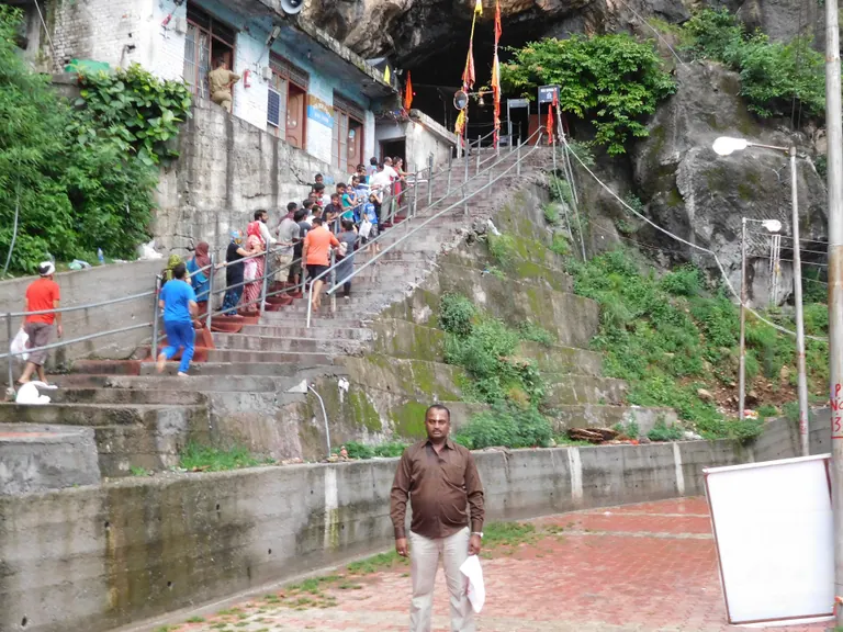 Pilgrims climbing stone steps beside rock walls and buildings at Shiv Khori in Reasi district