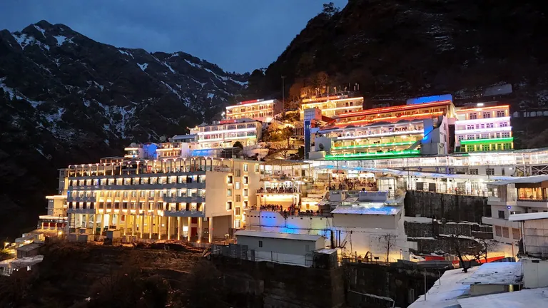The Vaishno Devi Bhawan buildings lit up in the evening against snowy mountains
