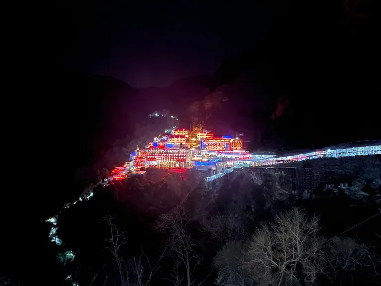 The Vaishno Devi Bhawan and the lit track glowing in colourful lights on the dark mountainside at night