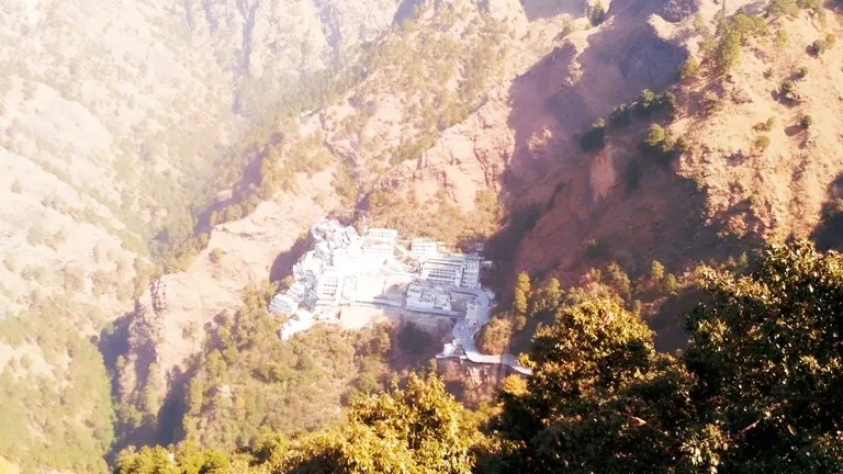 White buildings of the Vaishno Devi Bhawan set into a fold of the Trikuta mountain in warm light