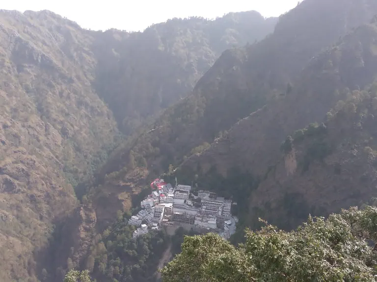 Panoramic view of a steep forested valley with the Vaishno Devi Bhawan buildings below the ridge