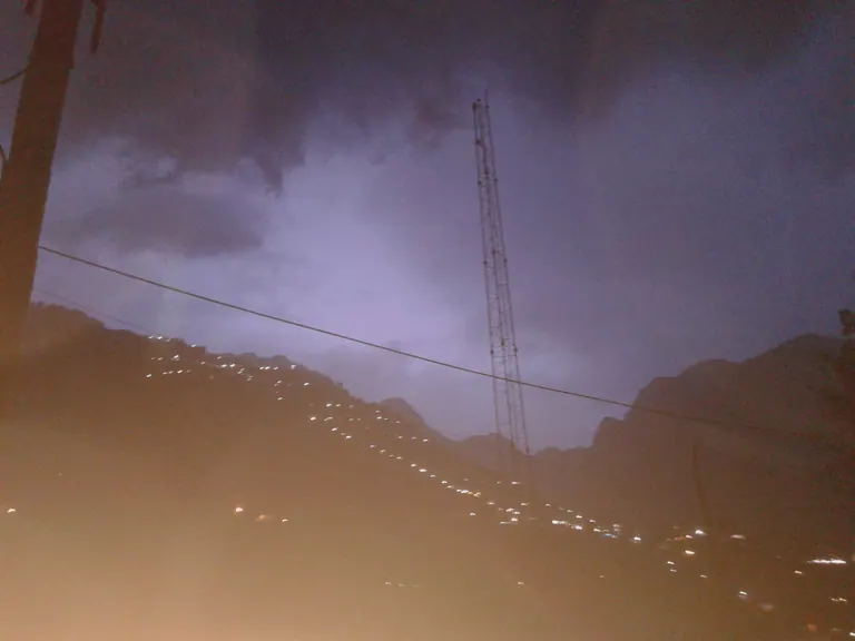 Heavy monsoon clouds over the hills on the Vaishno Devi route, with a line of track lights and a ropeway tower