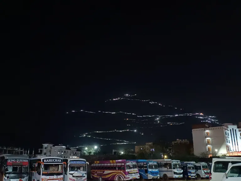 Zig-zag line of lights marking the Vaishno Devi track on the dark hillside above Katra, with buses parked in the foreground